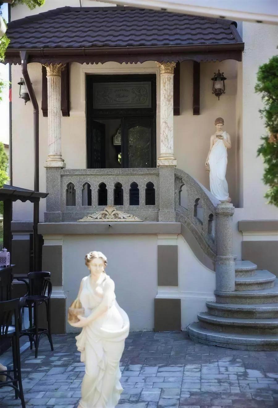 Intrarea în vila de epocă, cu trepte de piatră și o statuie albă