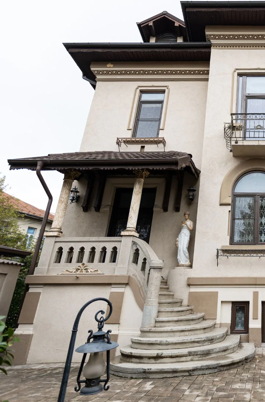 Intrarea în vila de epocă, cu trepte de piatră și o statuie albă